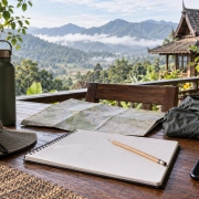 สมุดวางแผน แผนที่ หมวก ขวดน้ำ และโทรศัพท์บนโต๊ะริมระเบียงภูเขา